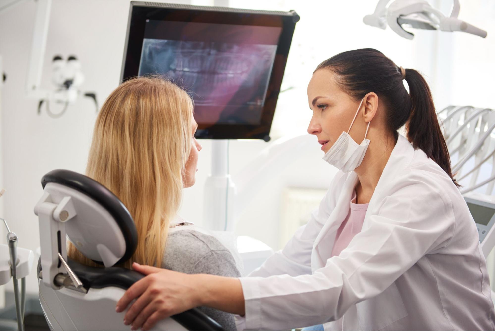 woman sitting in dental chair next to dentist who is comforting her