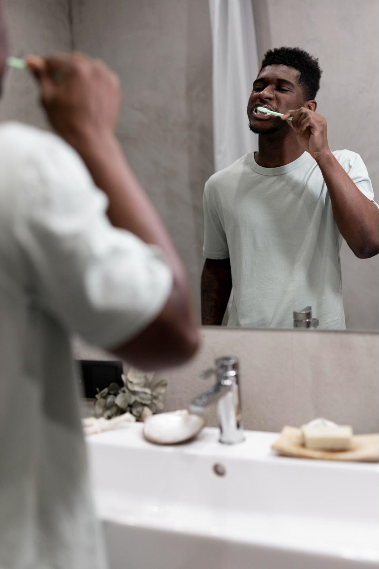 man brushing his teeth whilst looking in the mirror