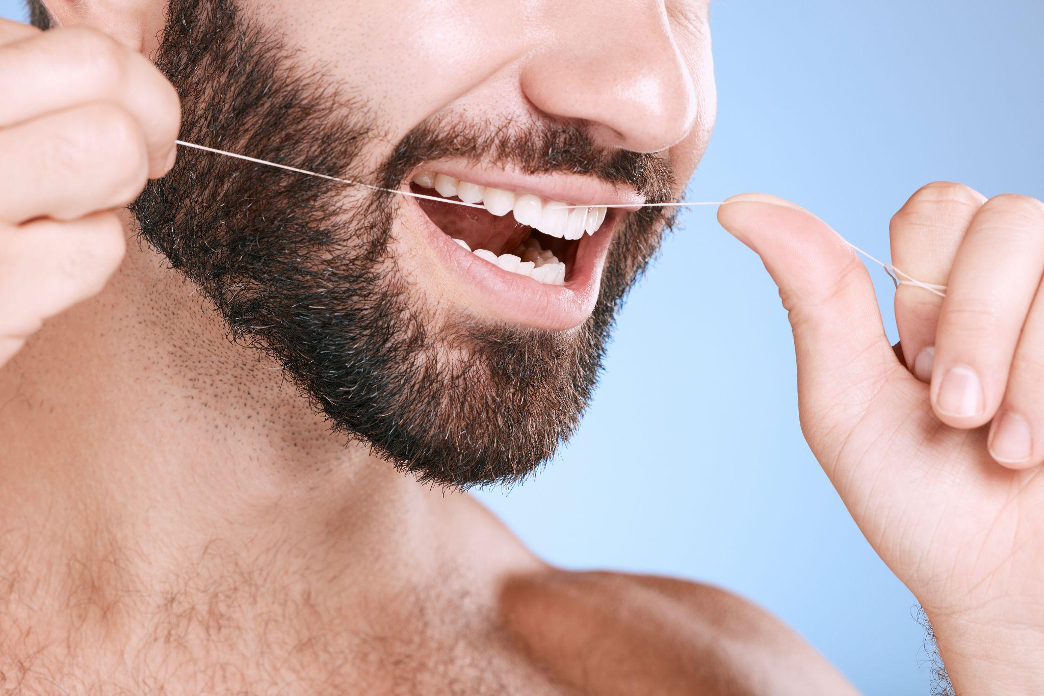 dental floss and oral hygiene with a man in studio on a blue background cleaning his teeth for healthy