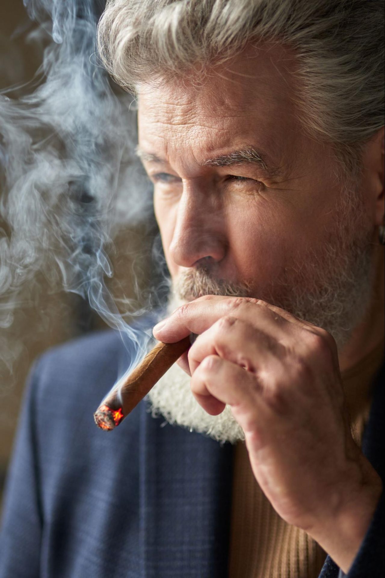 portrait of grey haired mature man looking away while smoking cigar