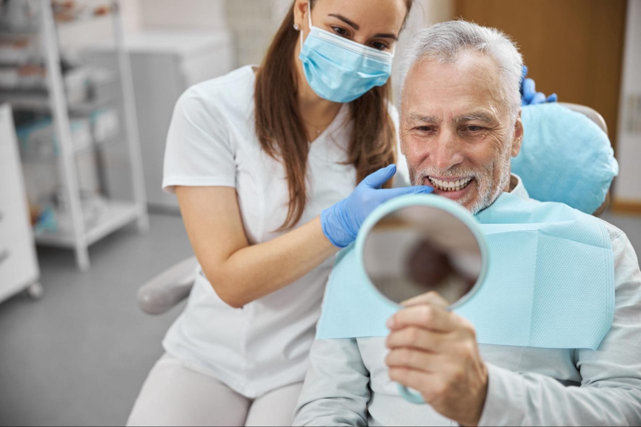 dentist with patient looking at mirror to see results