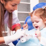 two years old girl is learning to brush her teeth with toothbrush in hand in the dental office