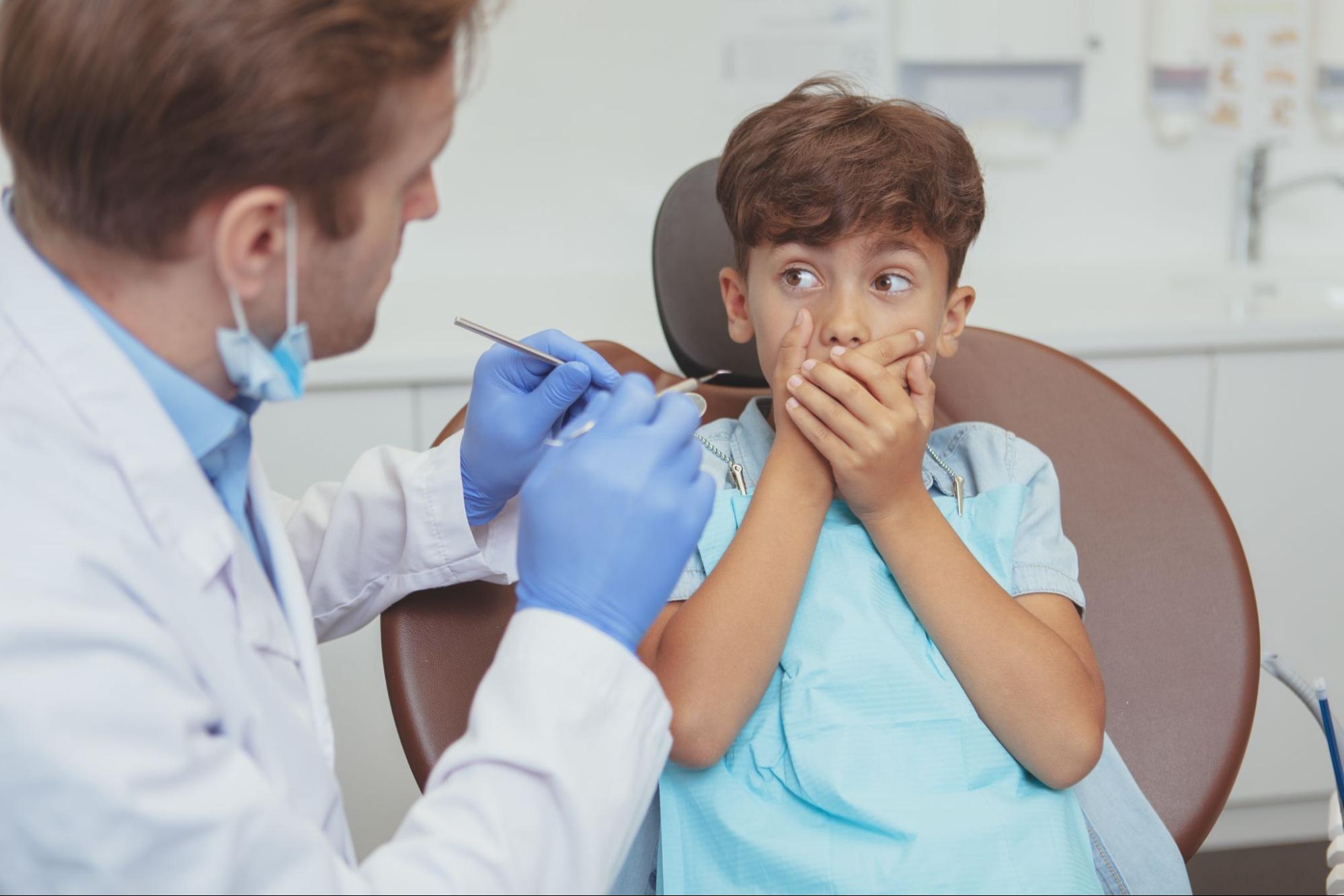 DENTIST WITH PATIENT SITTING IN CHAIR HOLDING HIS MOUTH CLOSED SHOWING HE IS SCARED OF DENTAL TREATMEN
