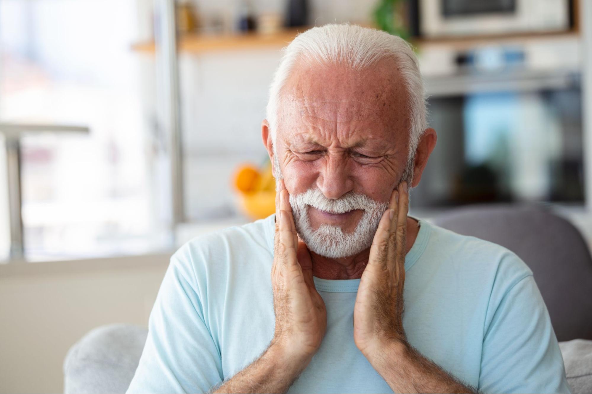 elderly man holding the sides of his face in pain